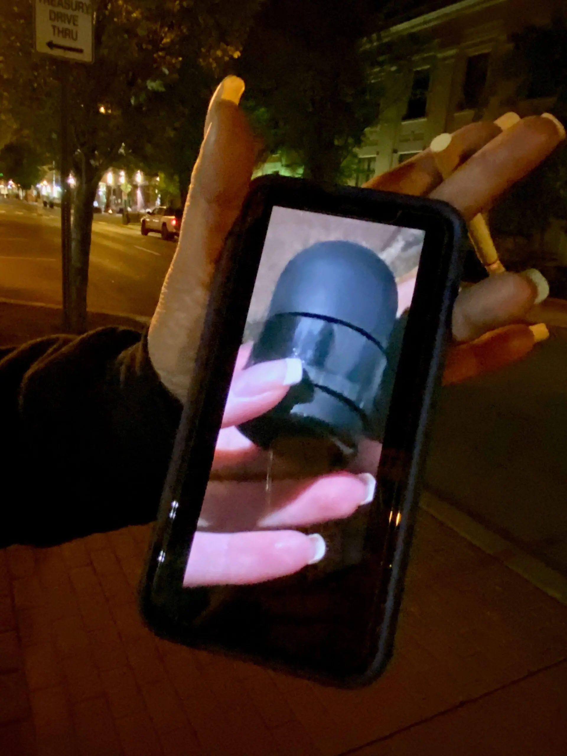A person holds a mobile phone displaying an image of a hand holding a rubber bullet.