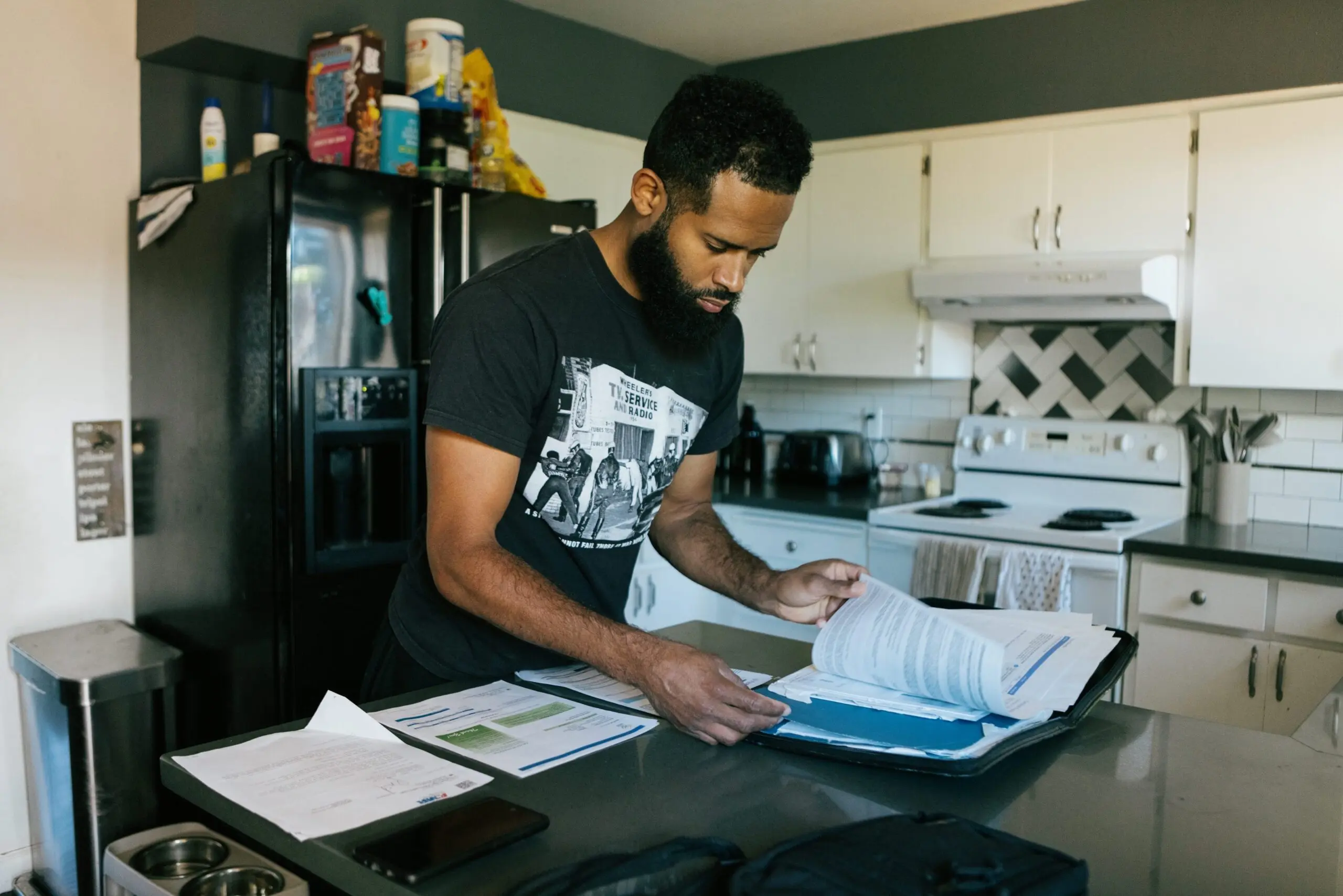 A man stands in his kitchen looking through paperwork.